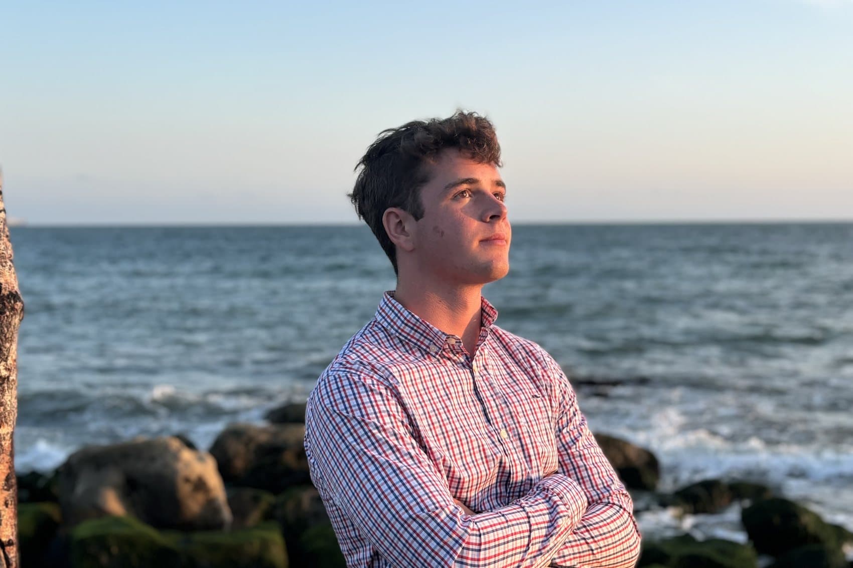 Charlie on a rocky shoreline at sunset, arms folded, looking out to sea